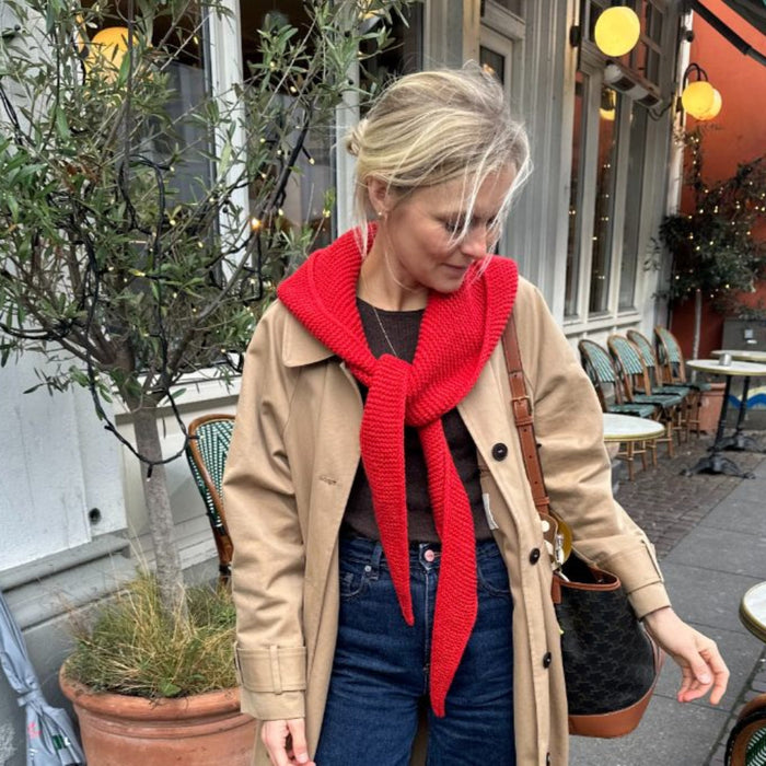 Woman wearing a cozy red Sophie Hood knitted scarf, perfect for winter layering, outside a café.