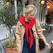 Woman wearing a cozy red Sophie Hood knitted scarf, perfect for winter layering, outside a café.