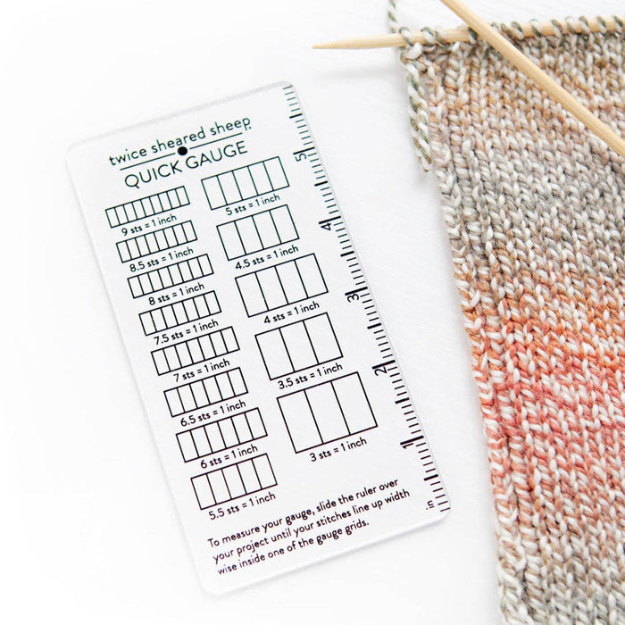 Quick Gauge ruler for measuring stitch gauge in knitting and crochet with multiple stitch count grids per inch next to knitted fabric and wooden knitting needles