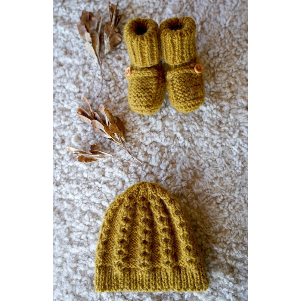 Flat lay of the golden cabled baby hat and button-tab boots — Vita Hat and Boots, Lisa F BC141.