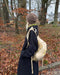Oslo Hat by PetiteKnit: brown knitted hat worn with a dark coat in an autumn garden